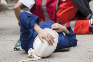 Person in hardhat lying on ground holding their head.